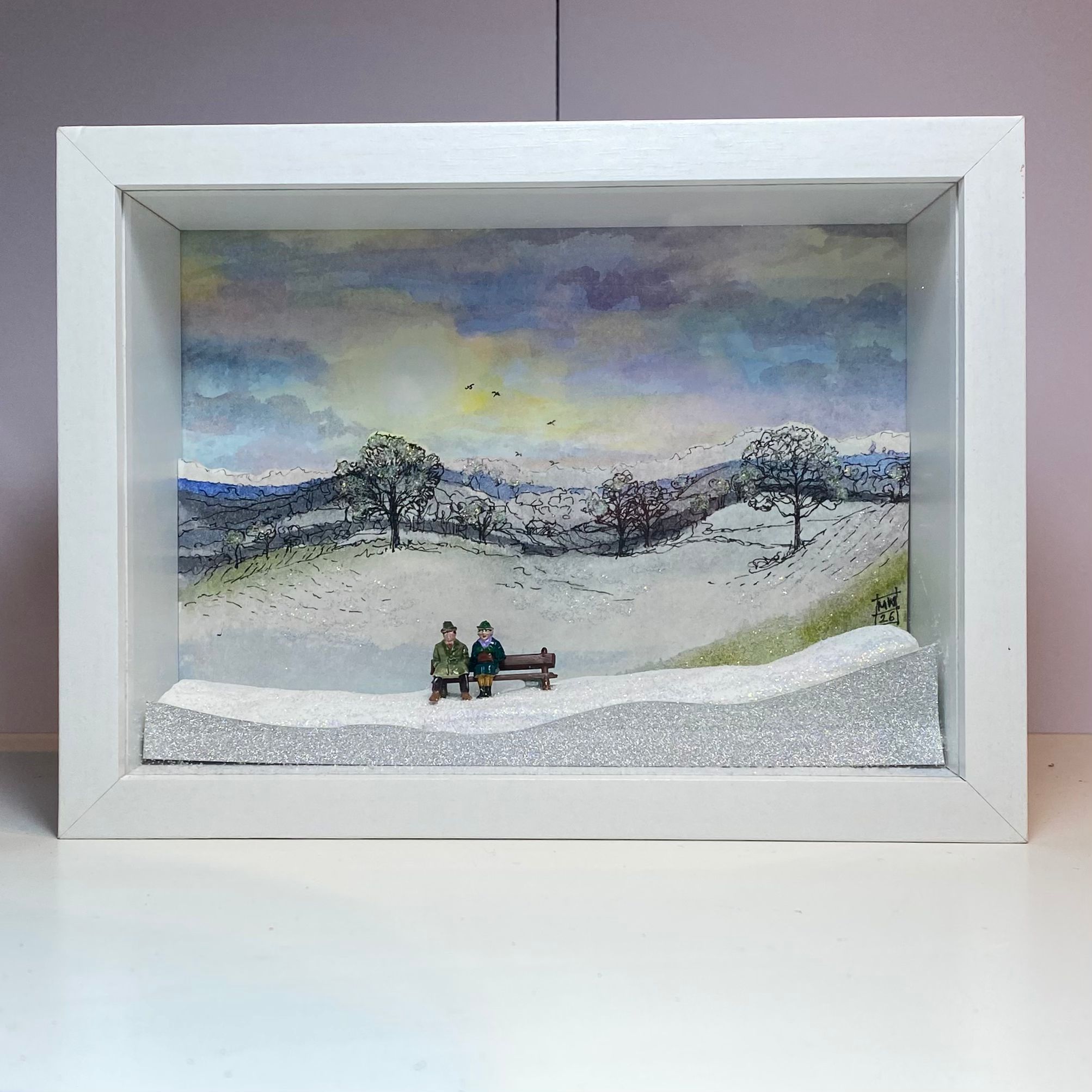 White frame with snowy scene inside, two people sitting on bench in snow
