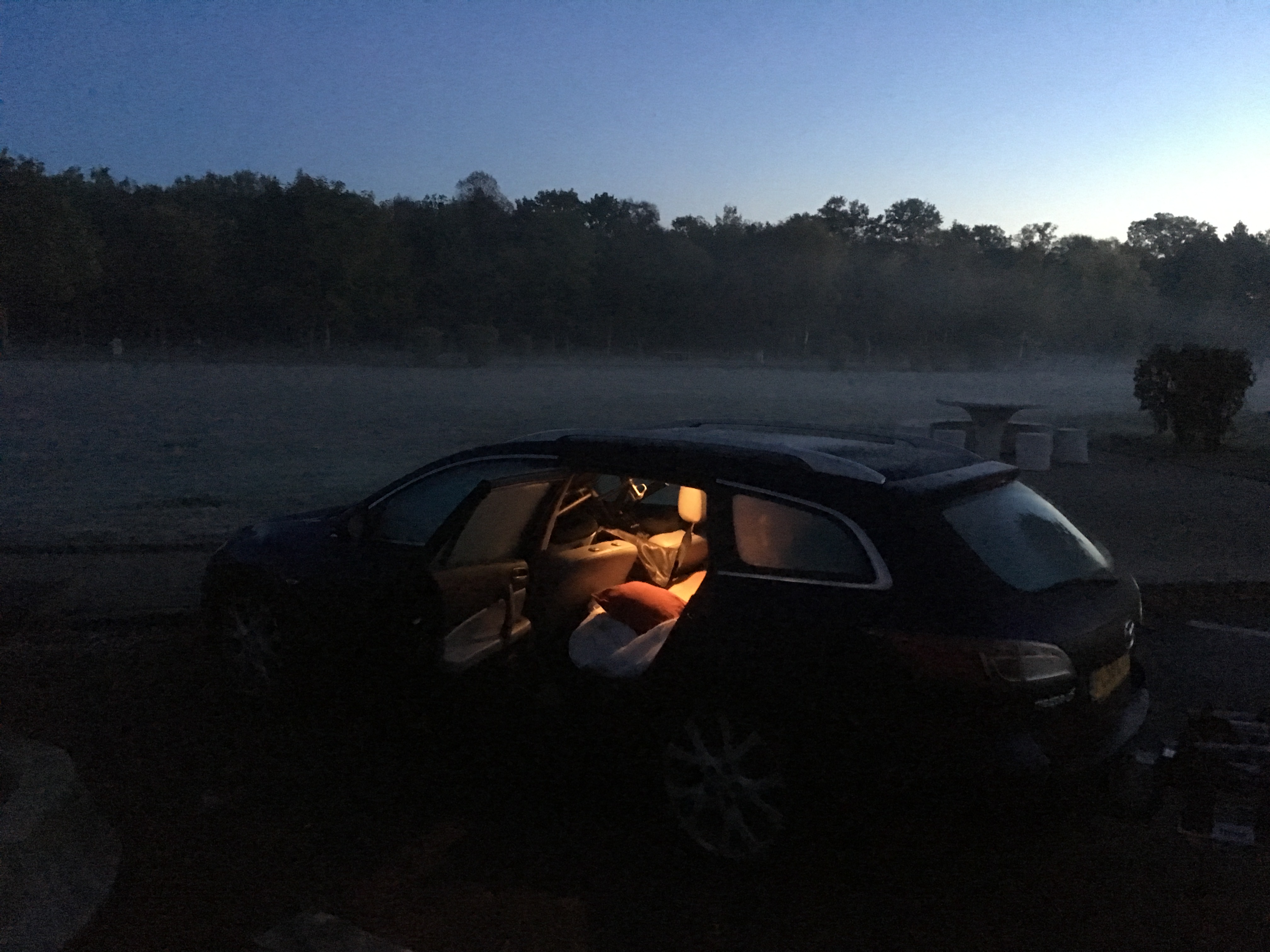 Photograph of a car with a bed inside it at sunset