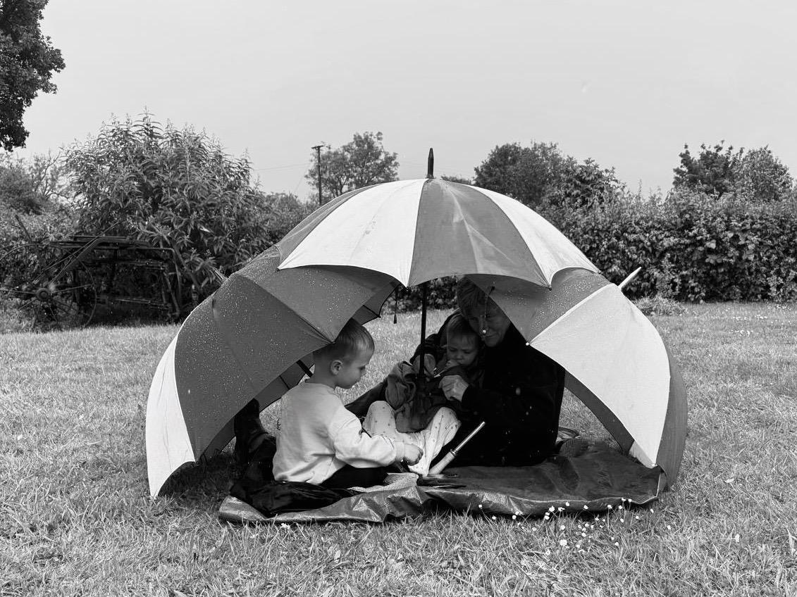 Black and white photo of kids under umbrellas with their grandparent