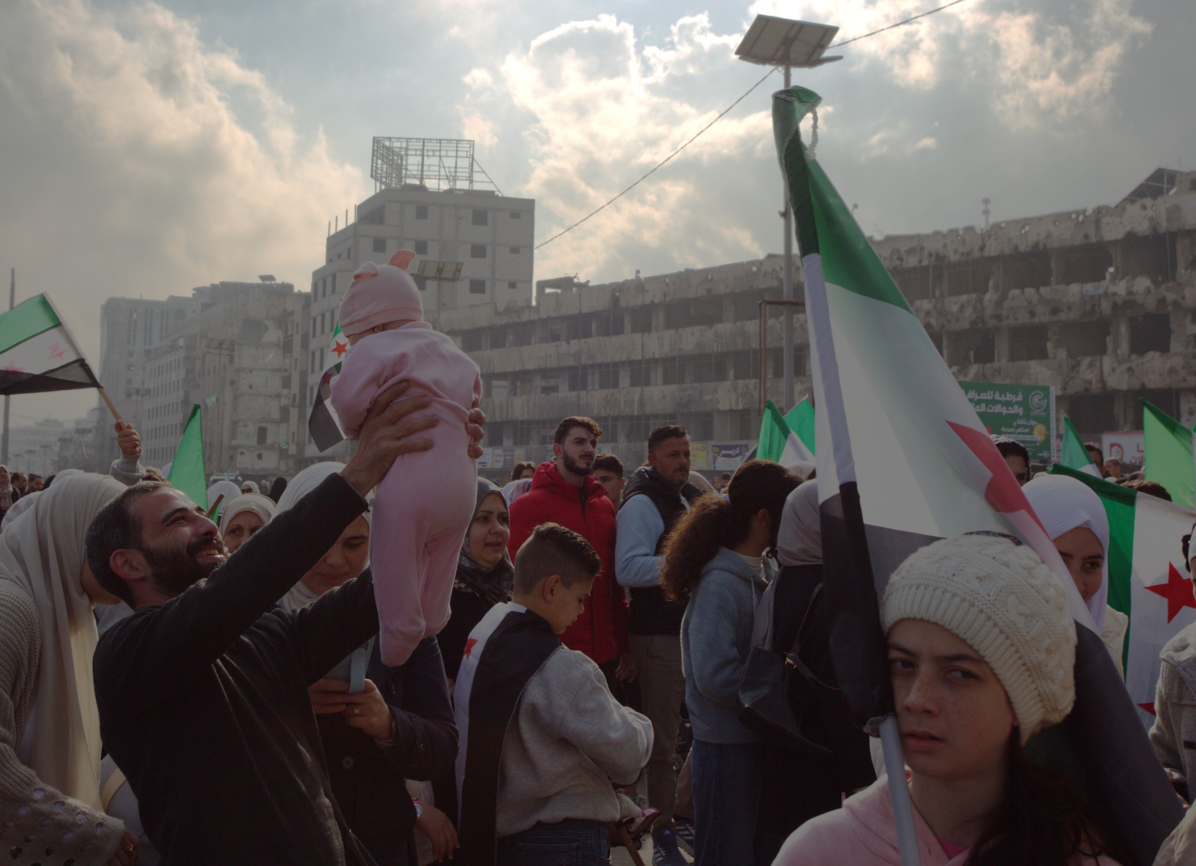 Photo of man holding a baby up in the air amongst a crowd