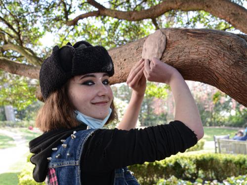 Secondary school student hanging clay artwork from a tree